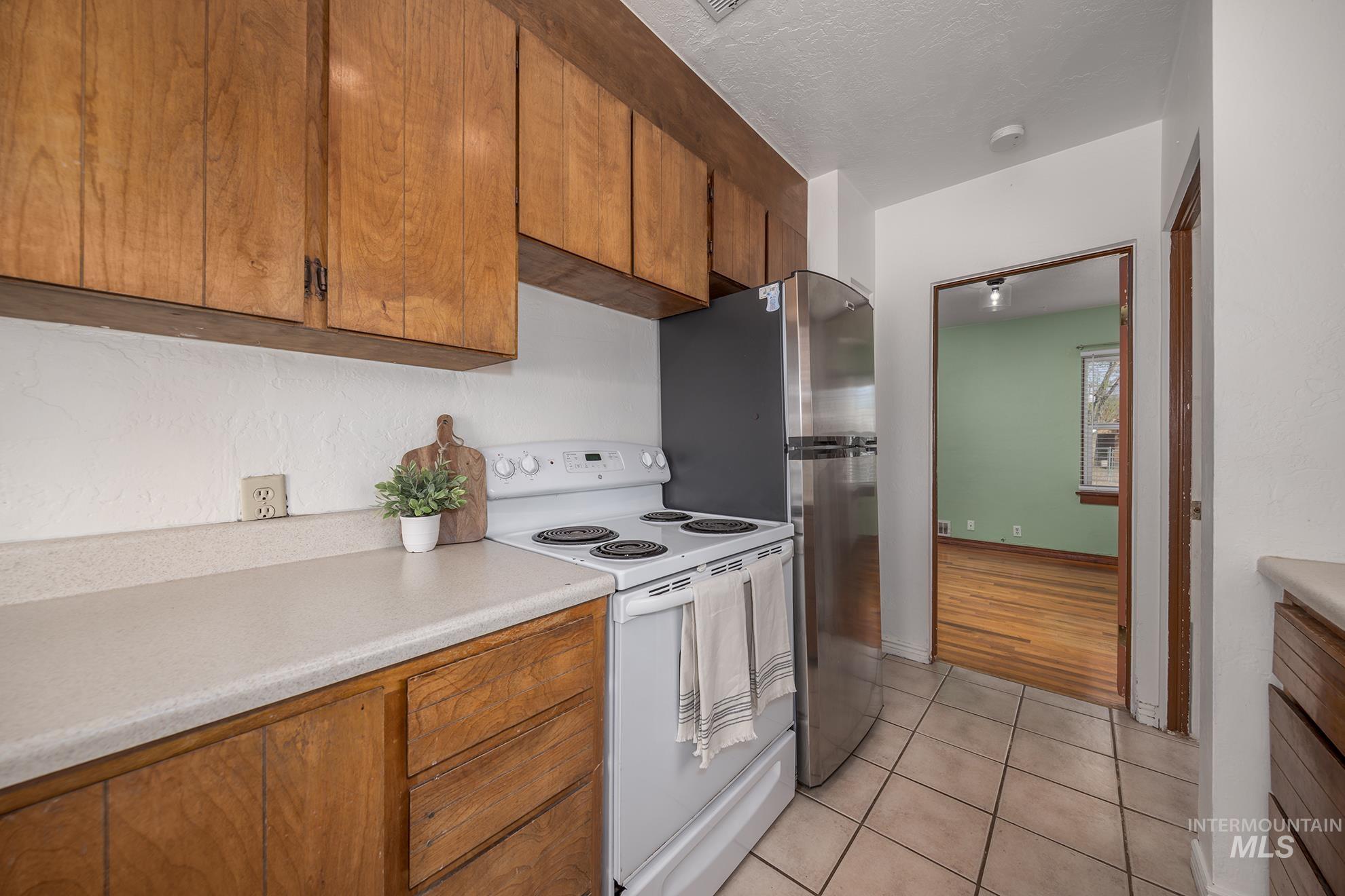 Kitchen with white electric range, wood finish cabinets, light countertops, light tile patterned flooring, and a textured ceiling