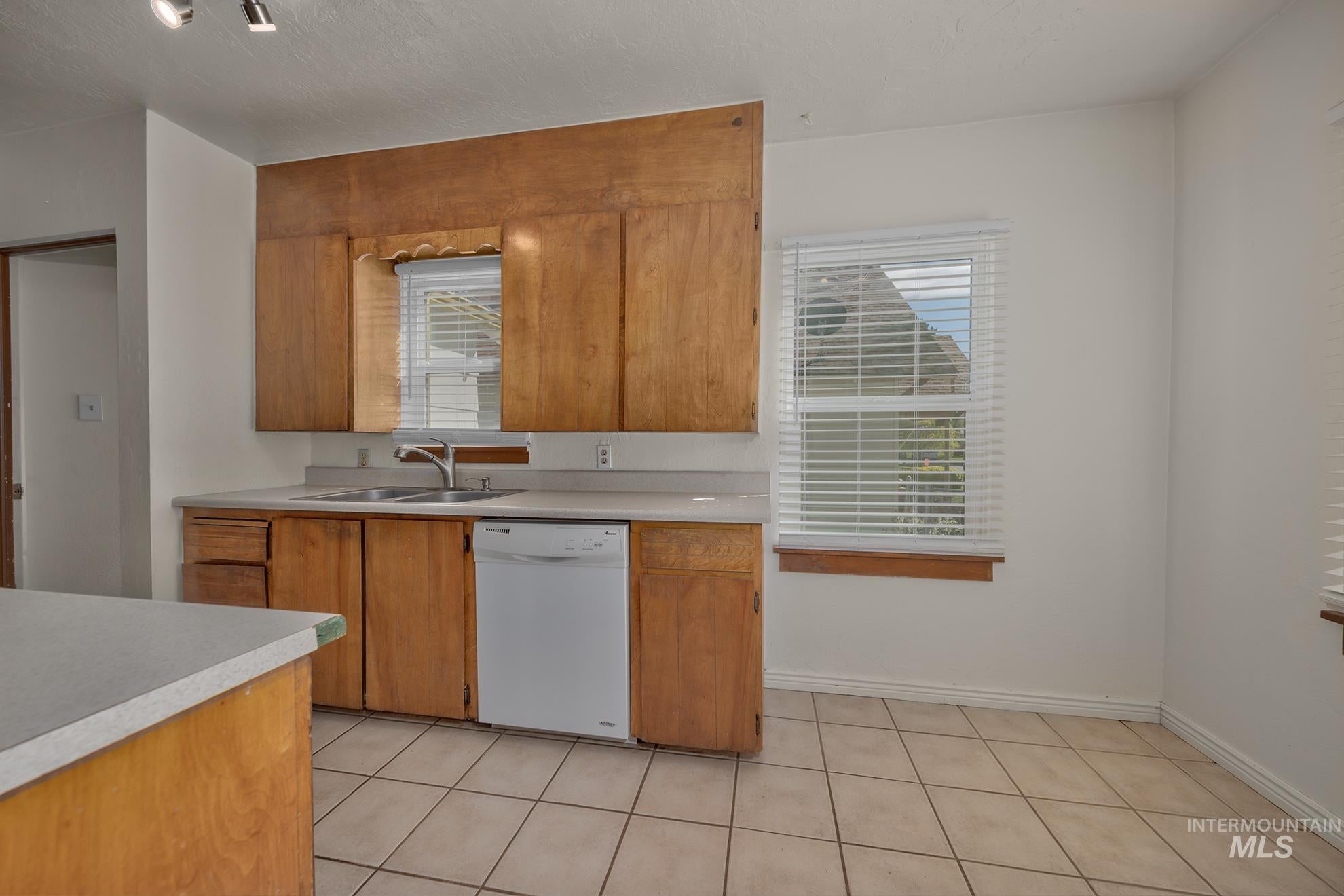 Kitchen with light countertops, dishwasher, wood finish cabinets, a textured ceiling, and light tile patterned floors