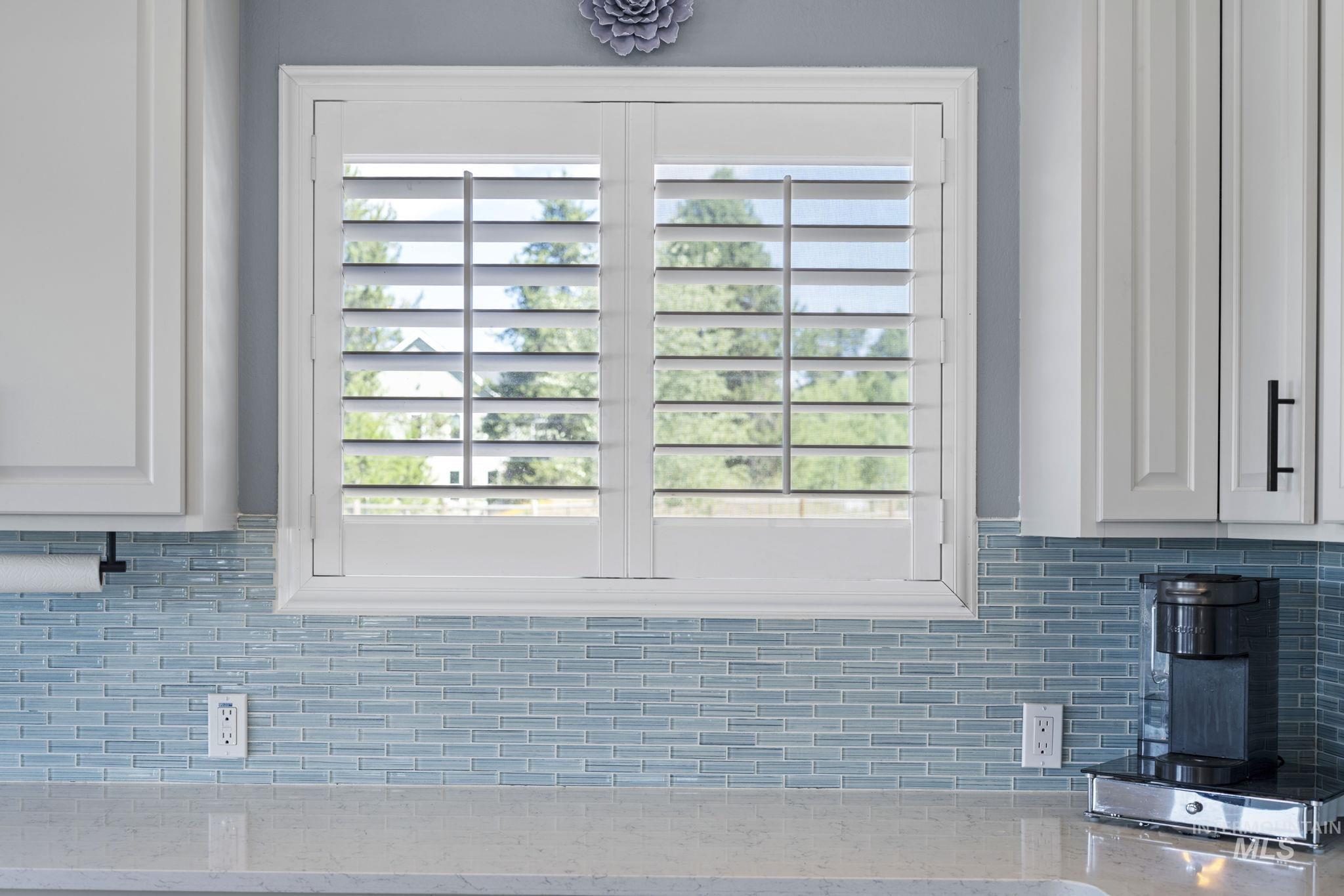 Kitchen view of decorative backsplash, white cabinets, and light stone counters