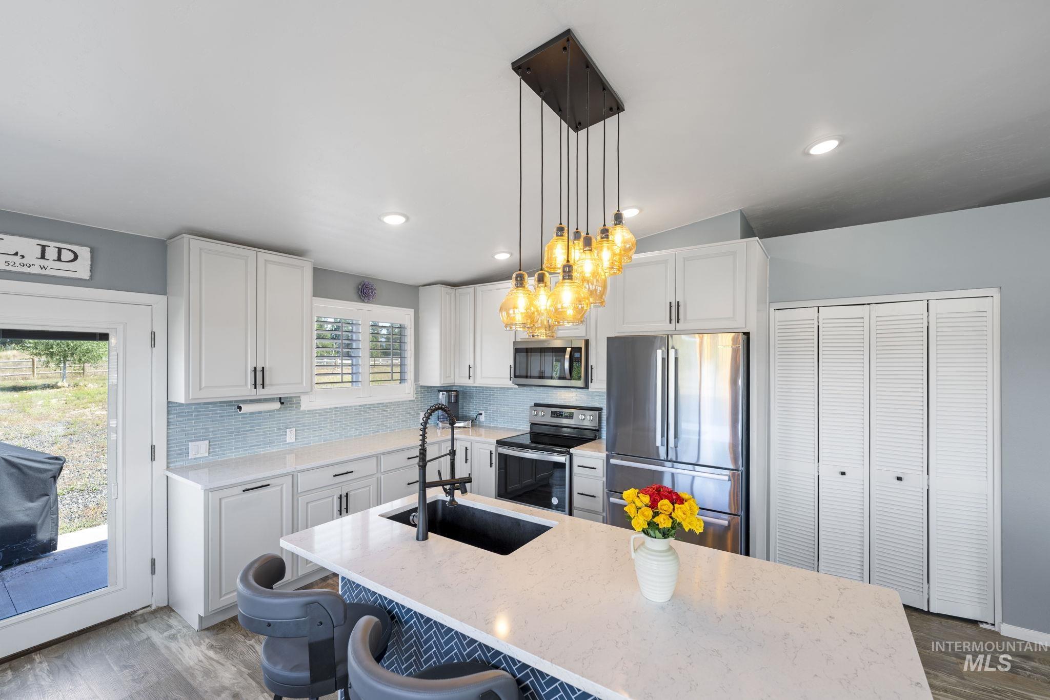 Kitchen featuring appliances with stainless steel finishes, dark wood finished floors, pendant lighting, white cabinets, and decorative backsplash