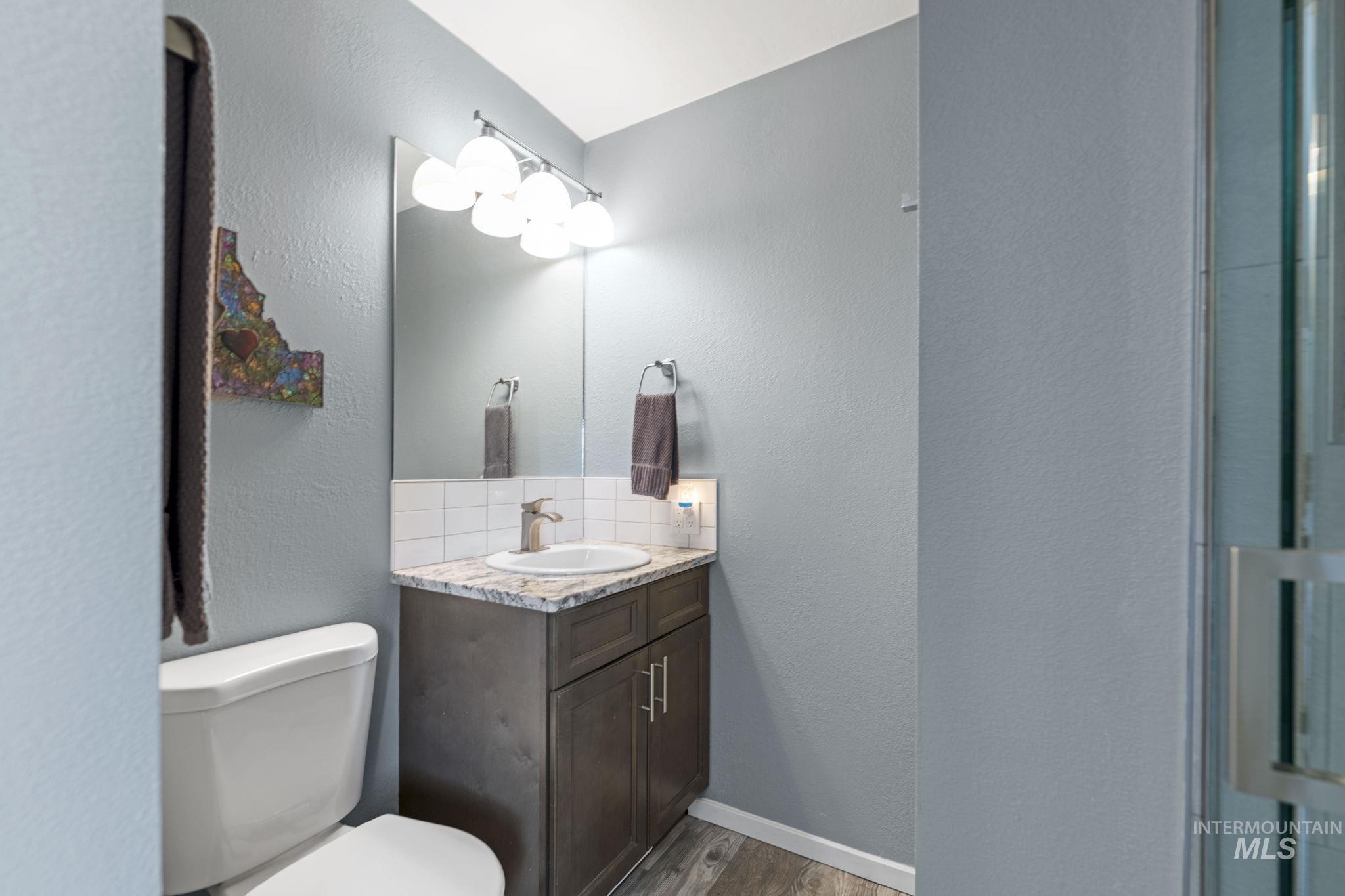 Bathroom featuring a textured wall, wood finished floors, tasteful backsplash, and vanity
