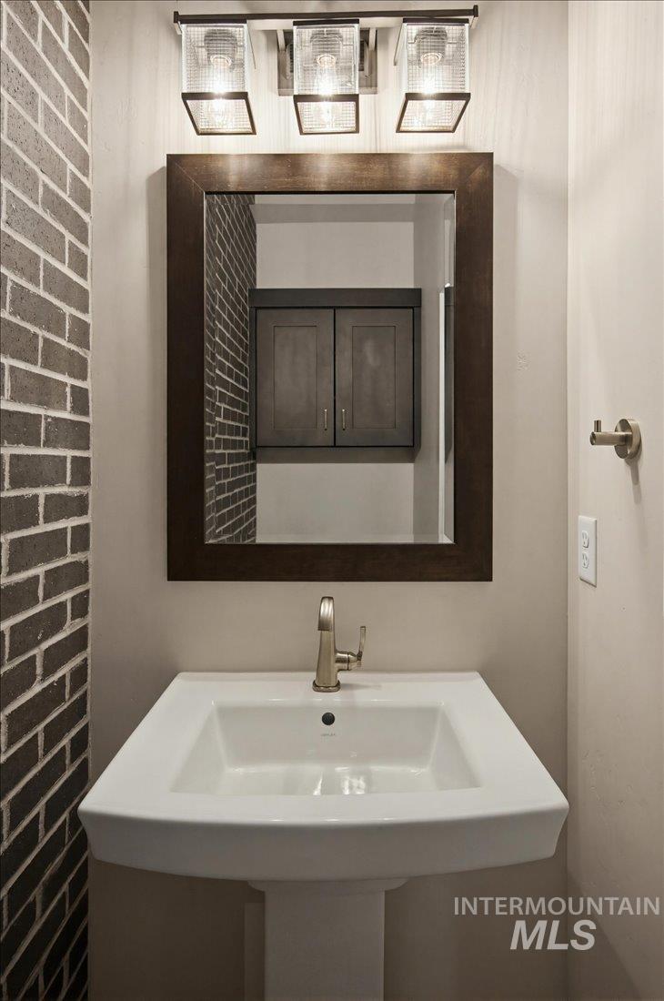 Pedestal sink with a brushed nickel faucet, framed mirror, and a three-light vanity fixture