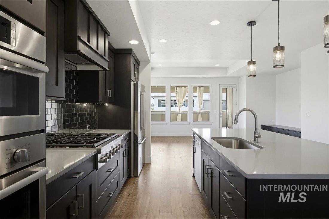 Spacious kitchen featuring dark wood cabinetry, stainless steel appliances, light-toned countertops, a tile backsplash, and wood-finish flooring