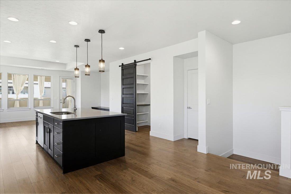 Open-concept interior featuring wood-finish flooring, a kitchen island with integrated sink, recessed lighting, and modern pendant lights