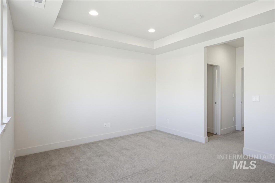Spacious room featuring light gray carpeting, crisp white walls, a tray ceiling with recessed lighting, and bright white trim