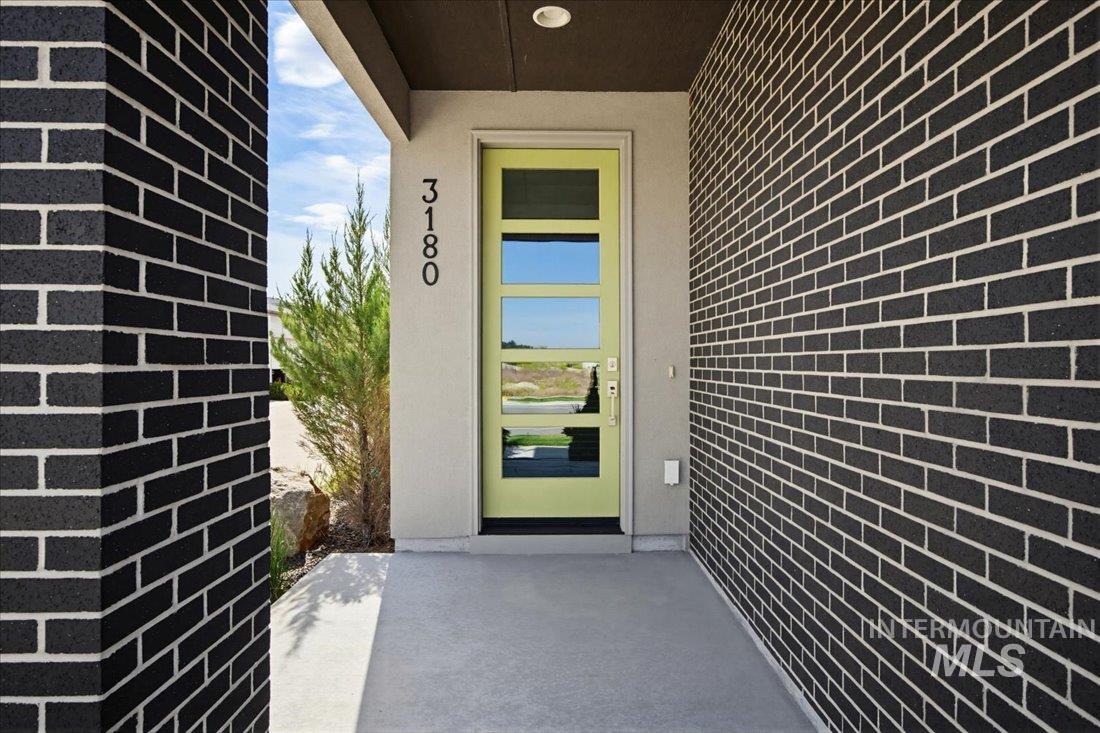 Contemporary entrance featuring a lime green paneled door with frosted glass inserts, dark brick exterior, concrete porch, and a recessed ceiling light fixture