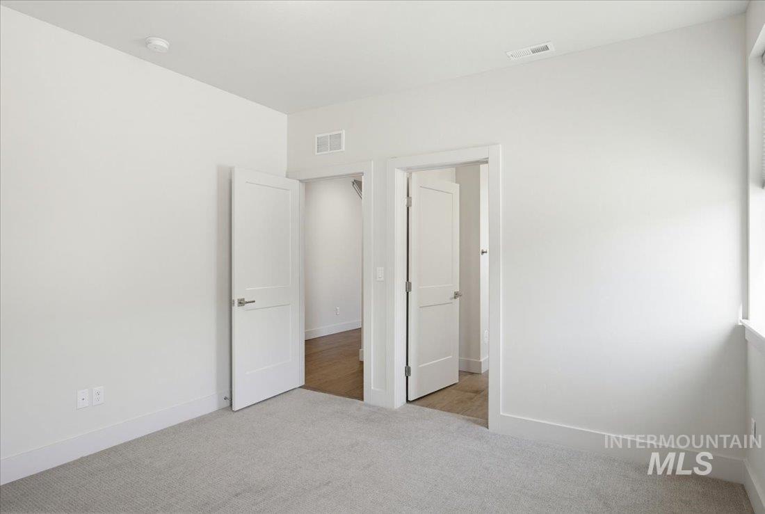 Neutral tone wall paint, light gray carpet flooring, white baseboards, and white paneled interior doors with brushed nickel hardware