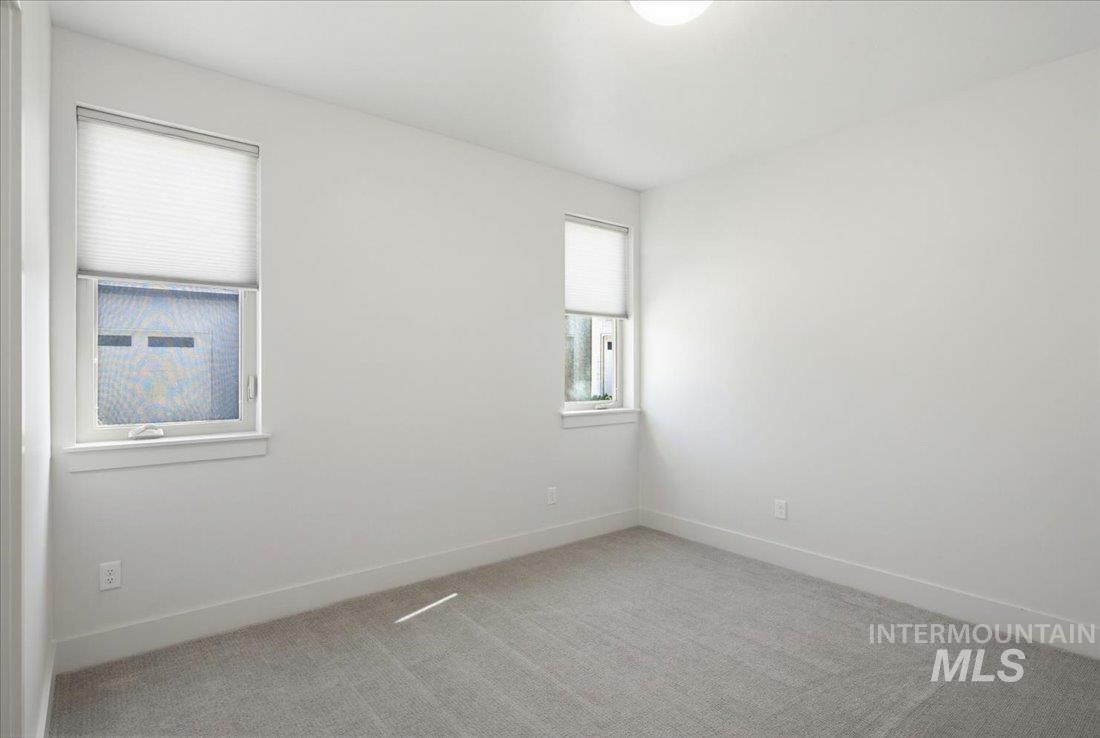 Neutral toned room featuring plush gray carpeting, two windows with white blinds, white trim, and a ceiling-mounted light fixture