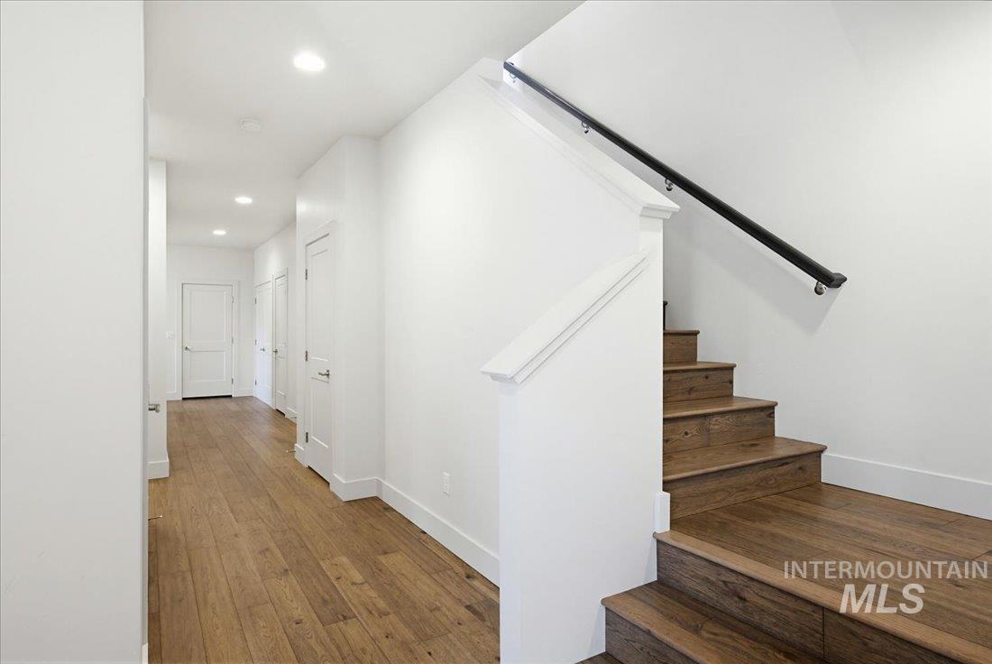 Hardwood staircase with a black metal handrail and white newel post, complementing the wood-finish flooring in the hallway