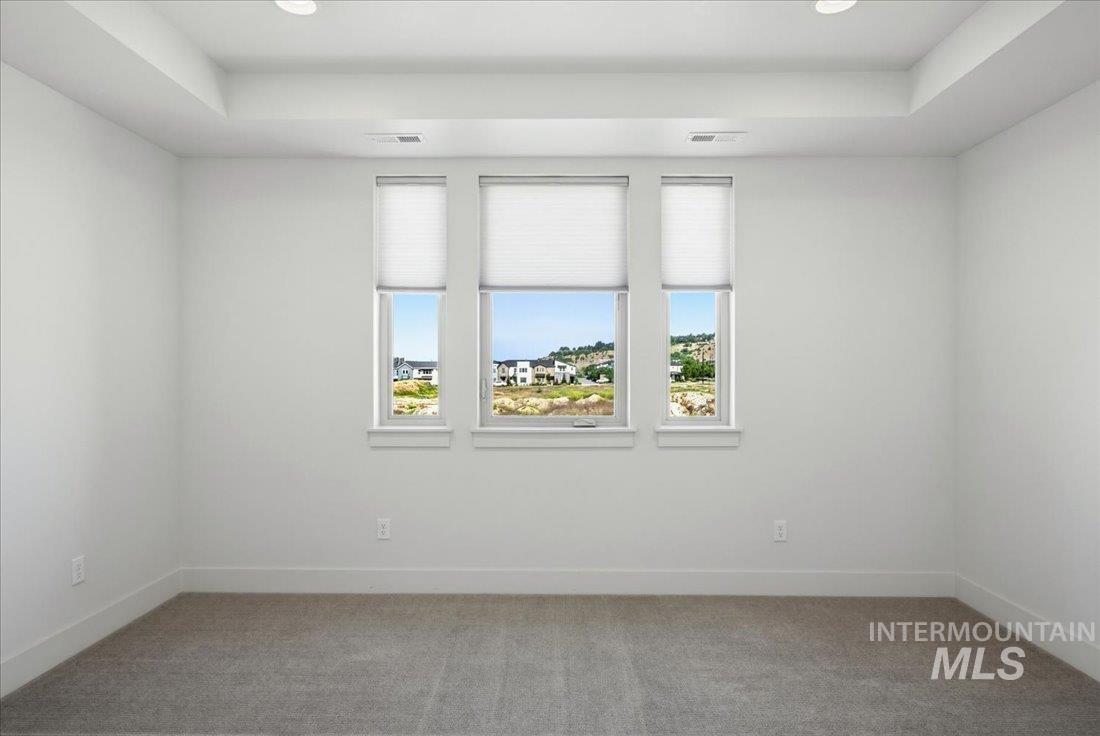 Room featuring three windows with blinds, a tray ceiling, recessed lighting, and grey carpet flooring