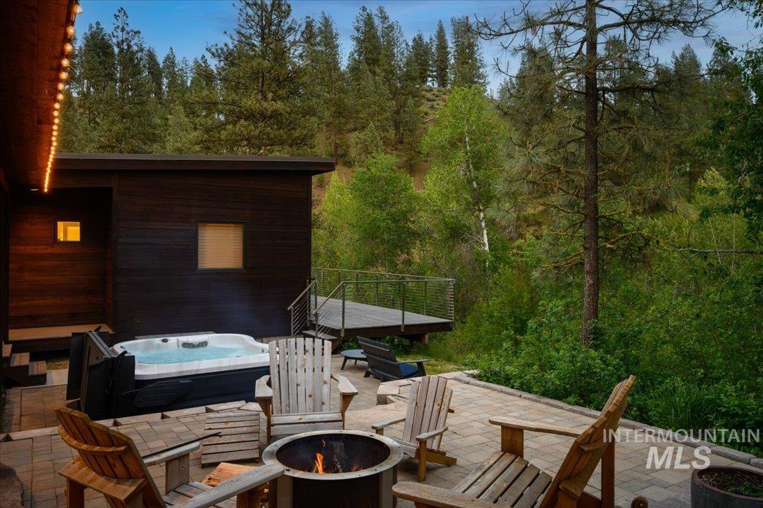 View of patio / terrace with an outdoor fire pit, a hot tub, a wooden deck, and a forest view