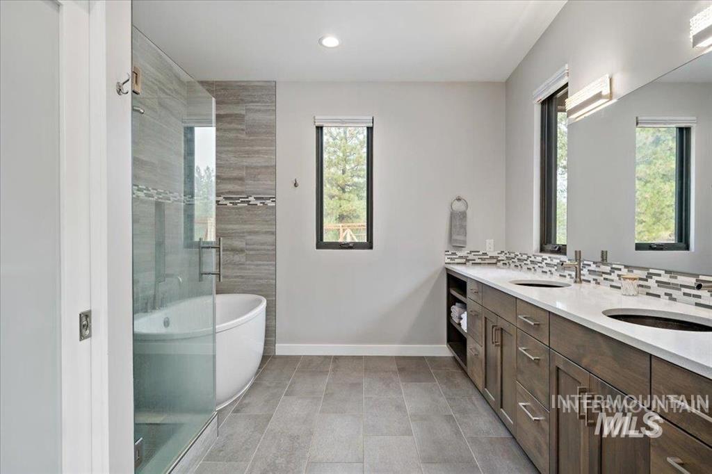 Bathroom featuring a freestanding bath, double vanity, recessed lighting, backsplash, and a tile shower