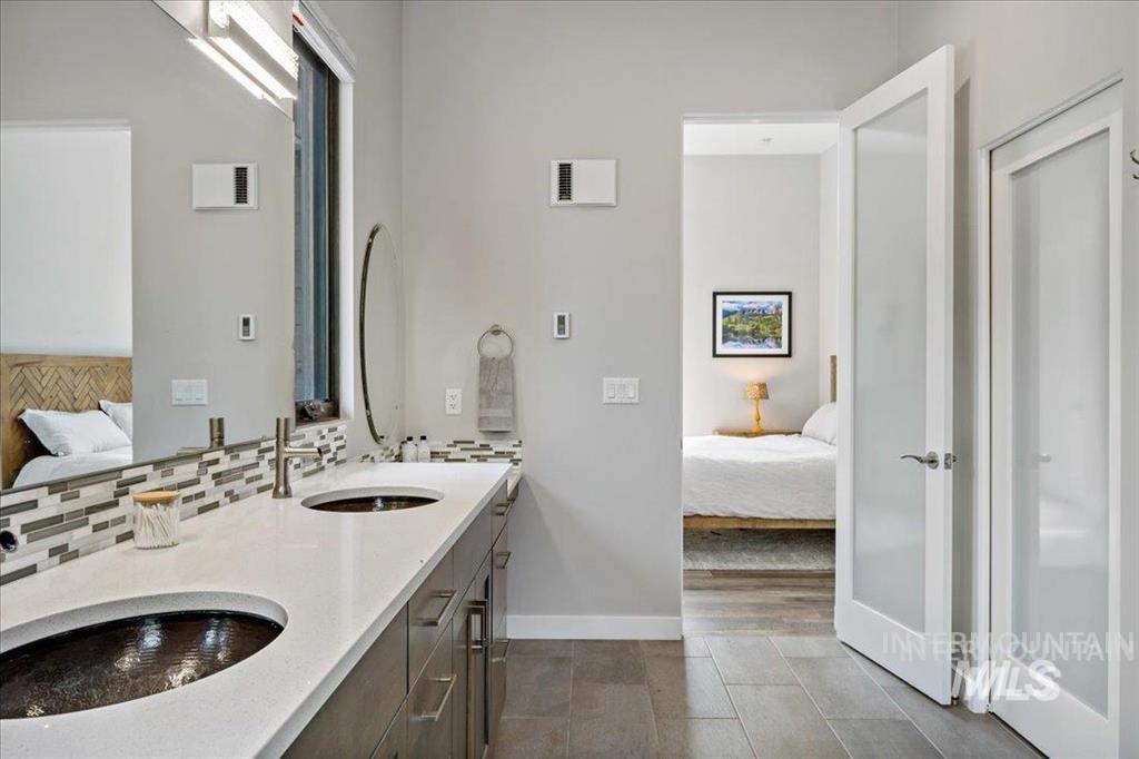 Full bath with connected bathroom, double vanity, dark tile patterned floors, and tasteful backsplash