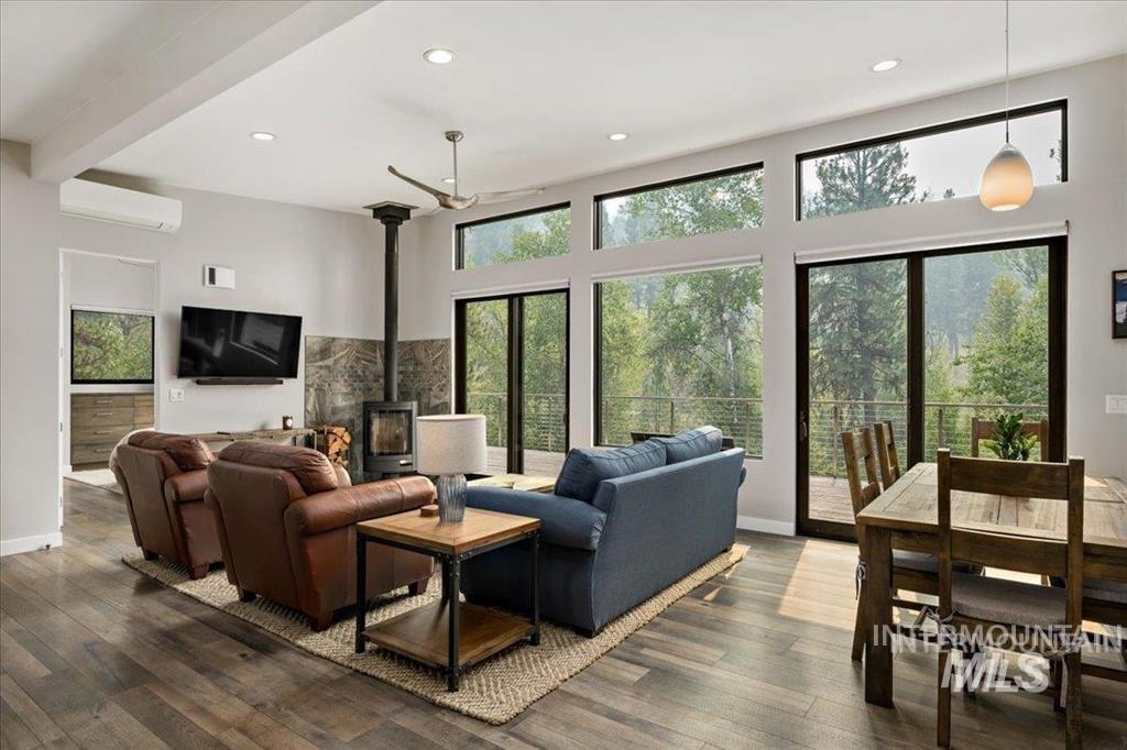 Living room with a wood stove, recessed lighting, hardwood / wood-style flooring, a wall mounted AC, and beam ceiling