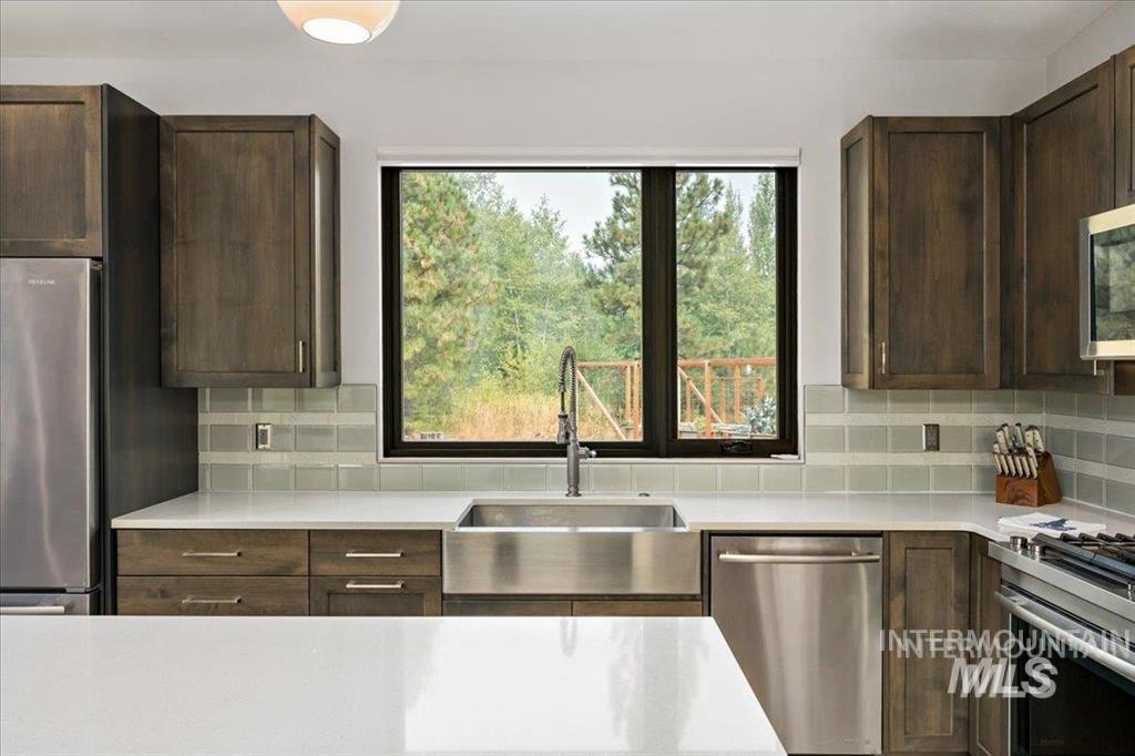 Kitchen with stainless steel appliances, tasteful backsplash, dark brown cabinets, and light stone countertops