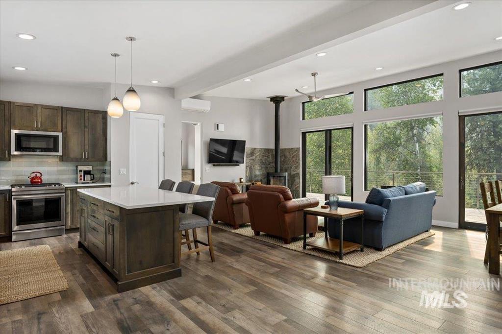 Kitchen featuring pendant lighting, beamed ceiling, dark brown cabinetry, a wood stove, and stainless steel appliances