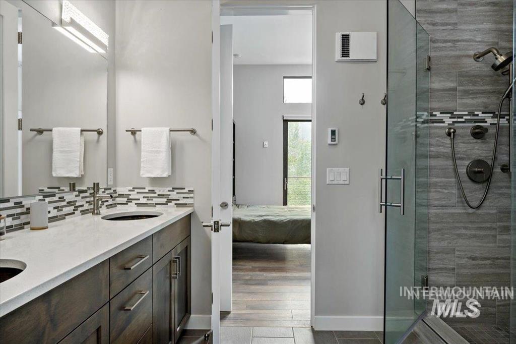 Full bathroom featuring a stall shower, double vanity, ensuite bath, decorative backsplash, and dark wood finished floors