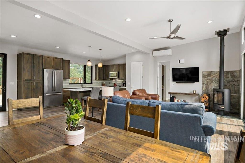 Living room featuring a wood stove, wood finished floors, recessed lighting, a ceiling fan, and beam ceiling