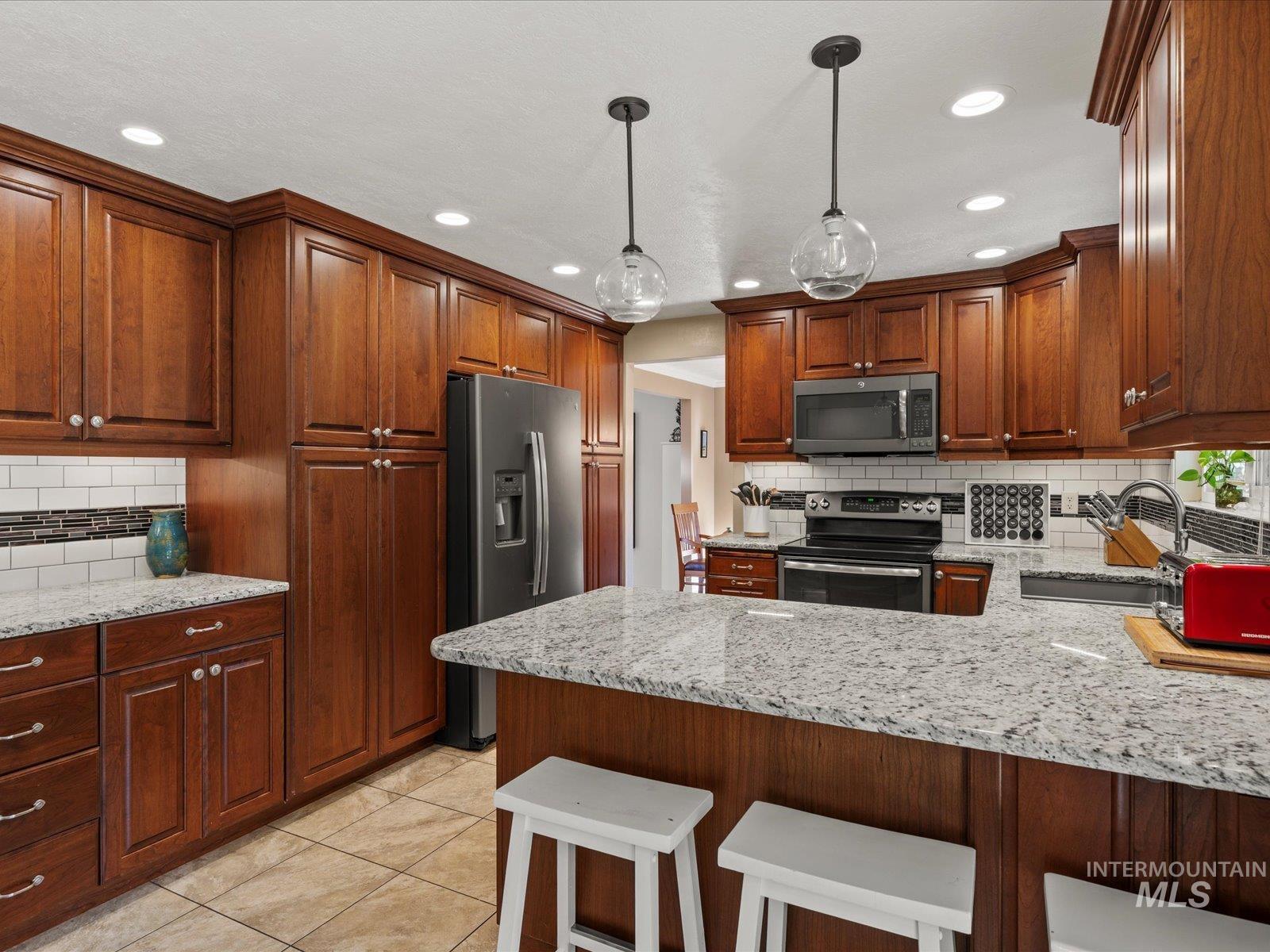 Kitchen with tasteful backsplash, light stone counters, a breakfast bar area, appliances with stainless steel finishes, and a peninsula