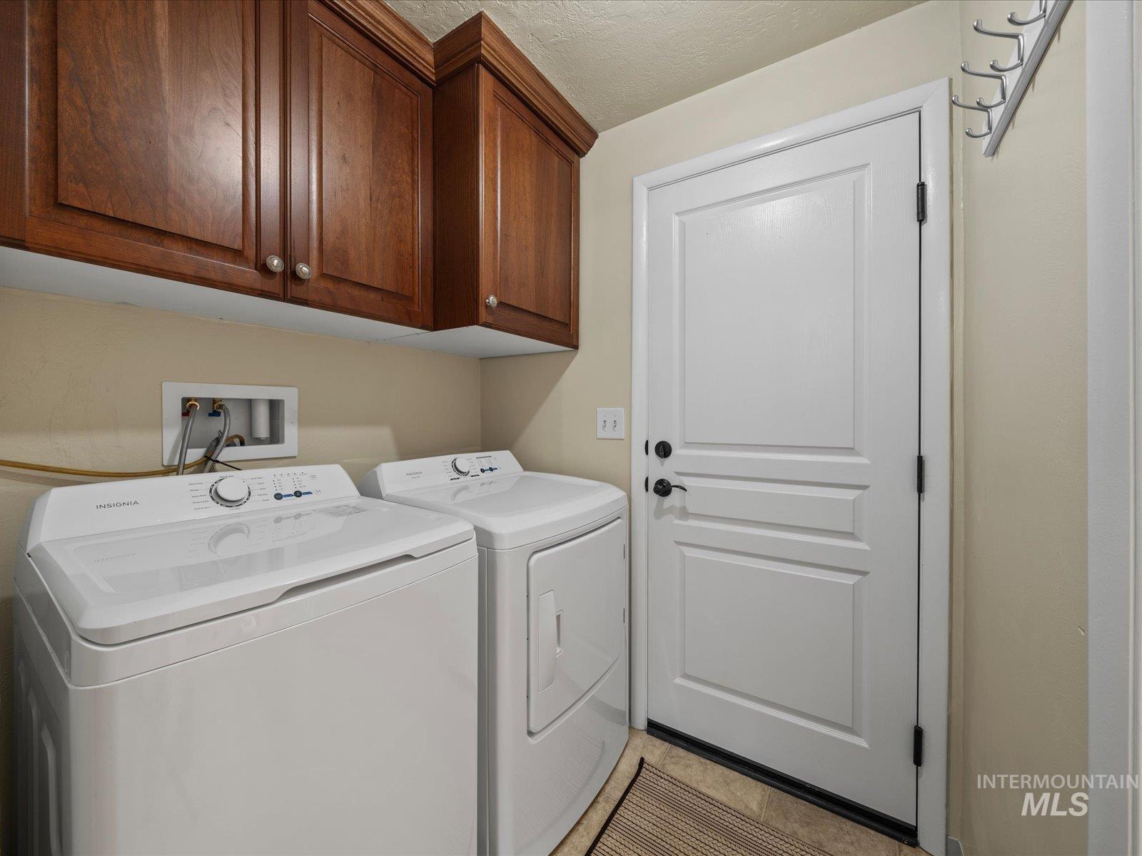 Laundry area with independent washer and dryer, cabinet space, a textured ceiling, and light tile patterned floors