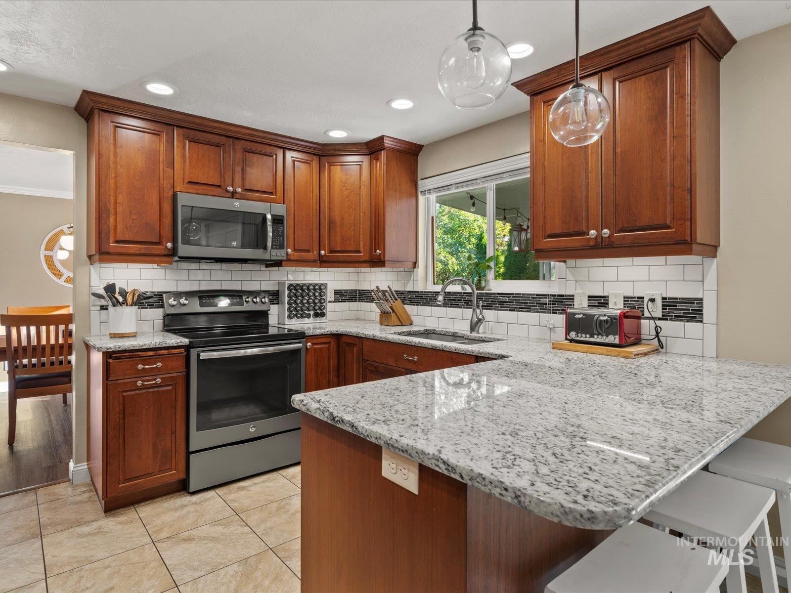 Kitchen featuring light stone counters, a kitchen breakfast bar, stainless steel appliances, a peninsula, and hanging light fixtures