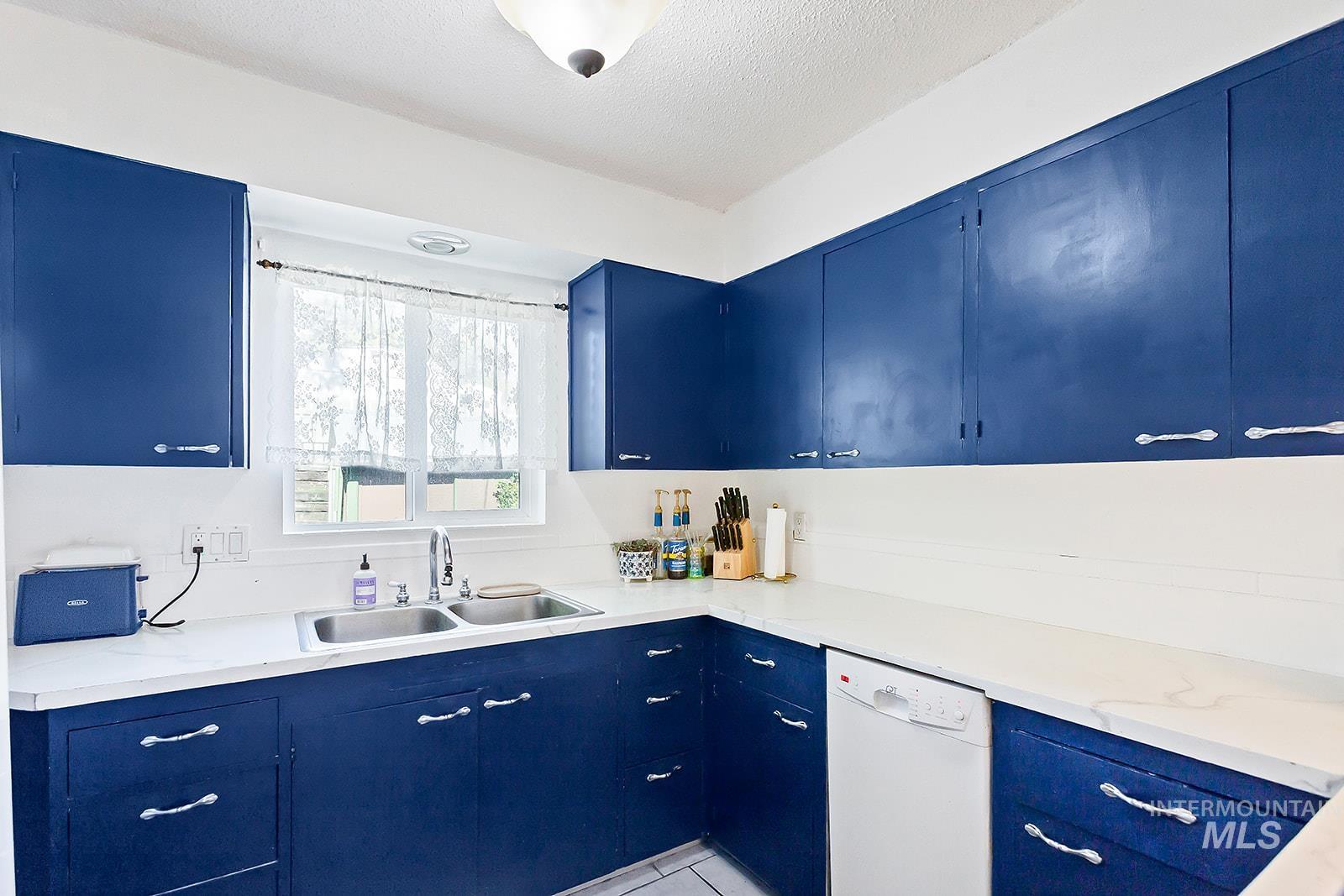 Kitchen featuring blue cabinetry, dishwasher, light countertops, a textured ceiling, and light tile patterned floors