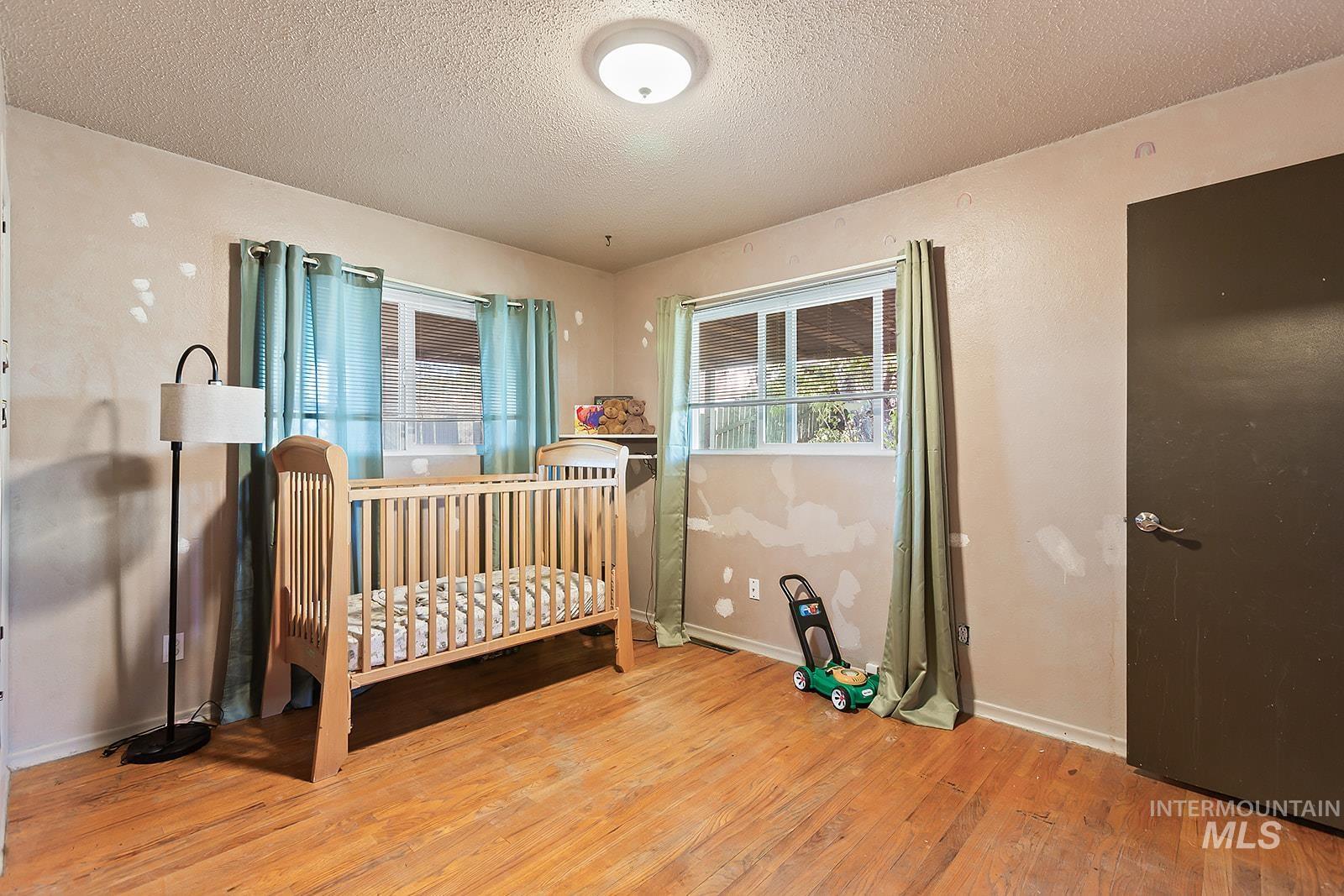 Bedroom with light wood-type flooring, a crib, and a textured ceiling
