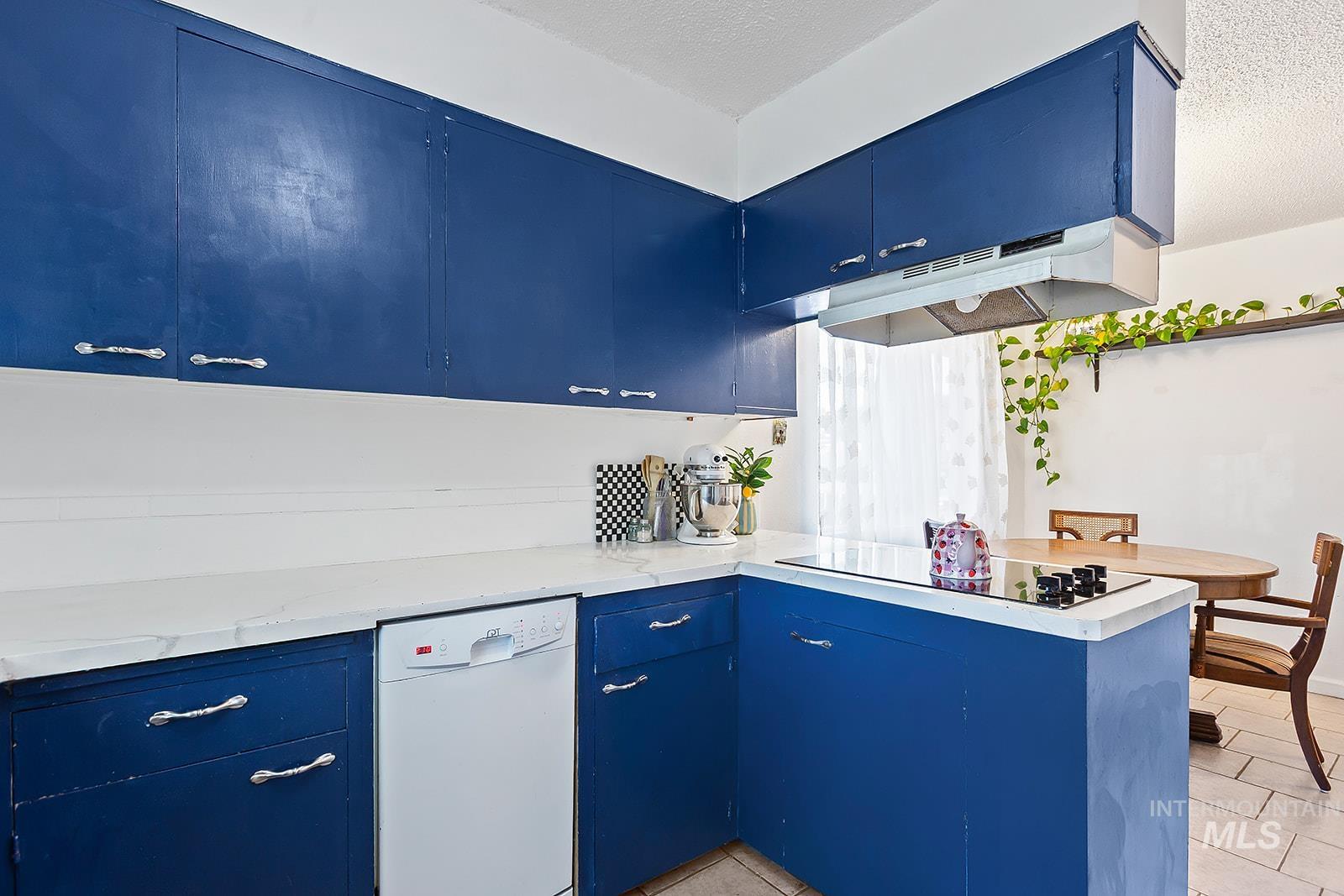 Kitchen with blue cabinetry, a peninsula, white dishwasher, light tile patterned floors, and a textured ceiling
