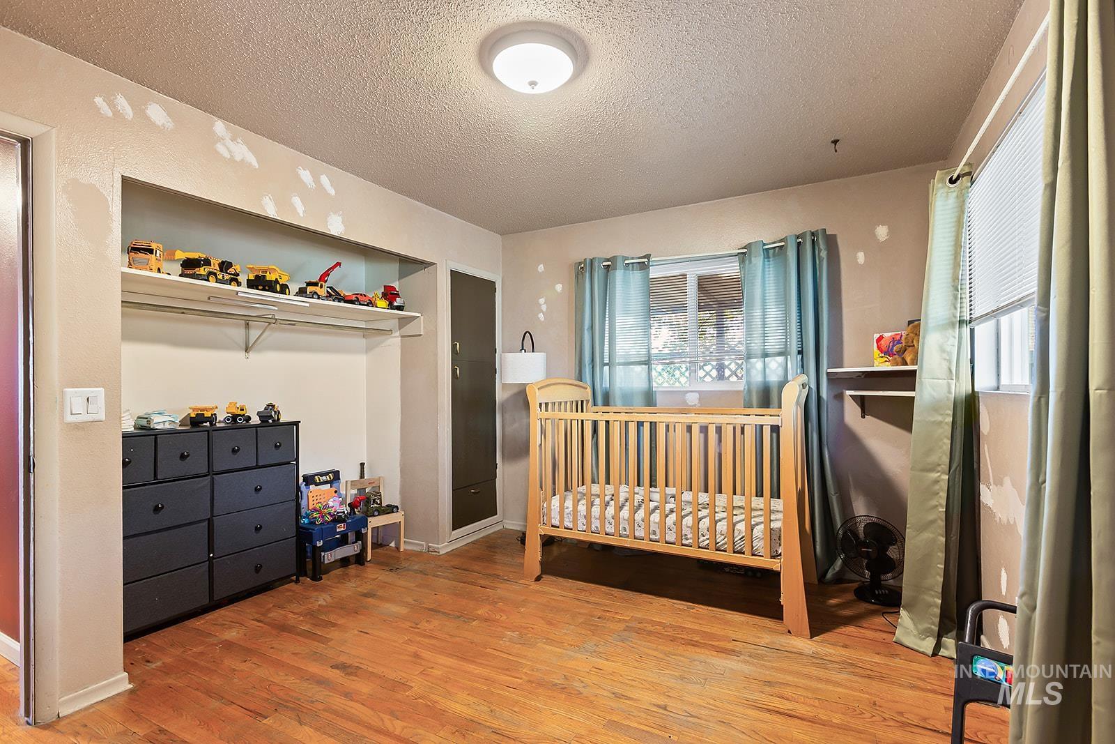 Bedroom with light wood-style floors, a crib, a textured ceiling, and multiple windows