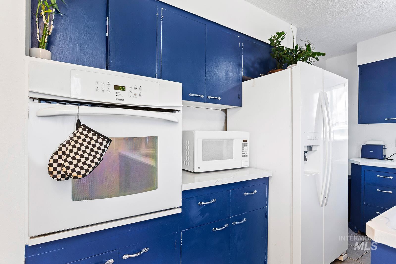 Kitchen featuring blue cabinets, white appliances, light countertops, and a textured ceiling
