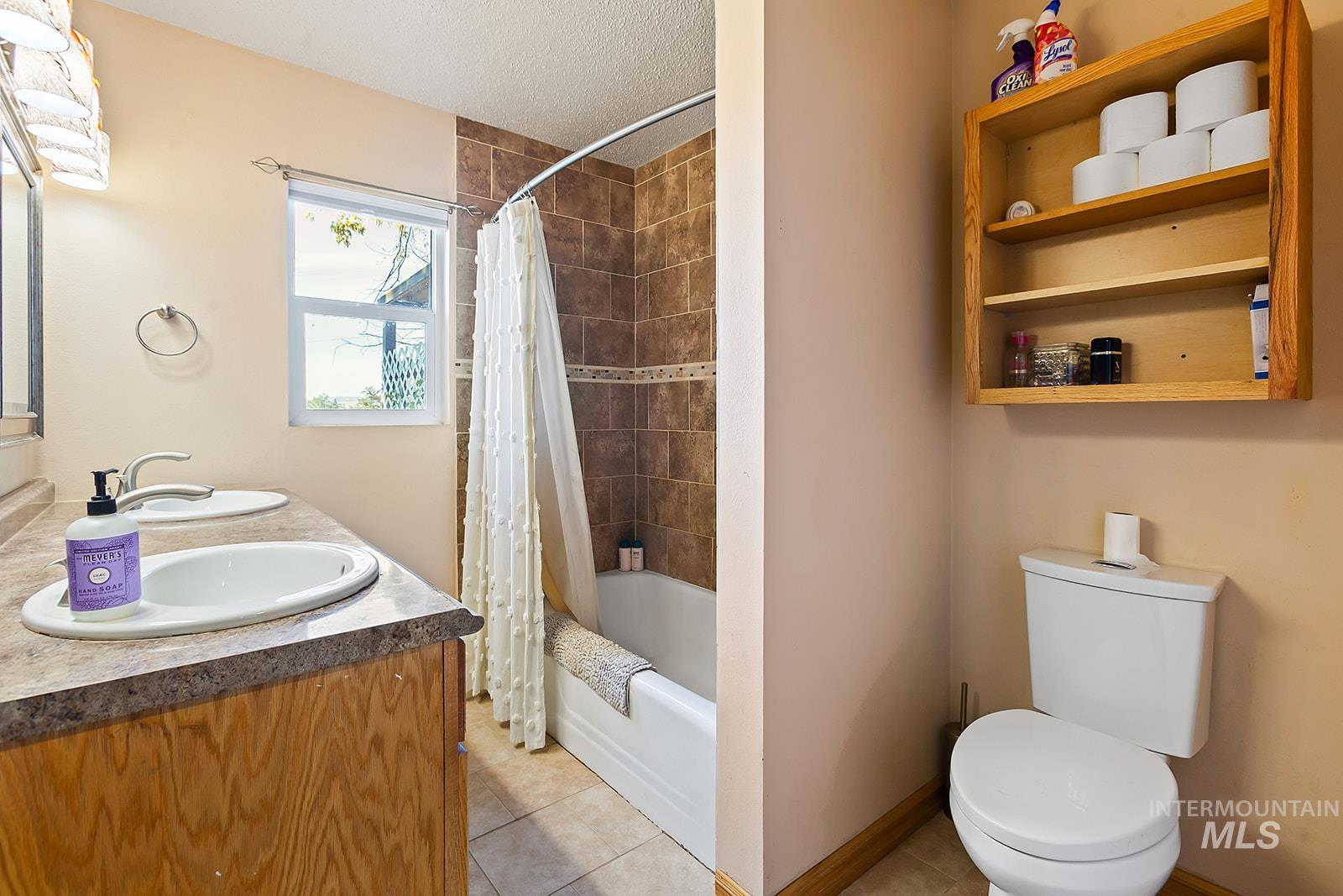 Bathroom featuring light tile patterned floors, shower / tub combo, a textured ceiling, and double vanity