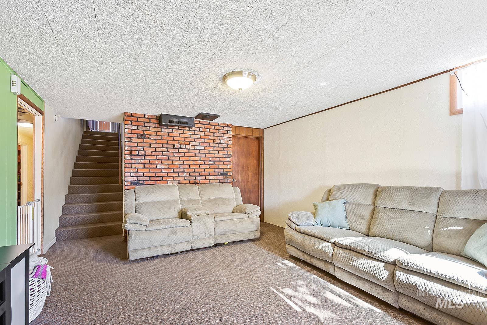 Living room with carpet, stairs, wood walls, and a textured ceiling