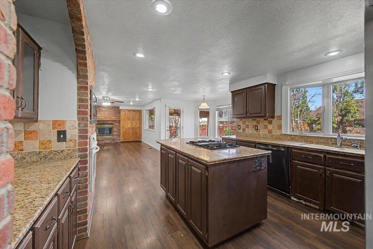 Kitchen featuring backsplash, a kitchen island, dark wood finish cabinetry, a brick fireplace, and dark wood-style floors