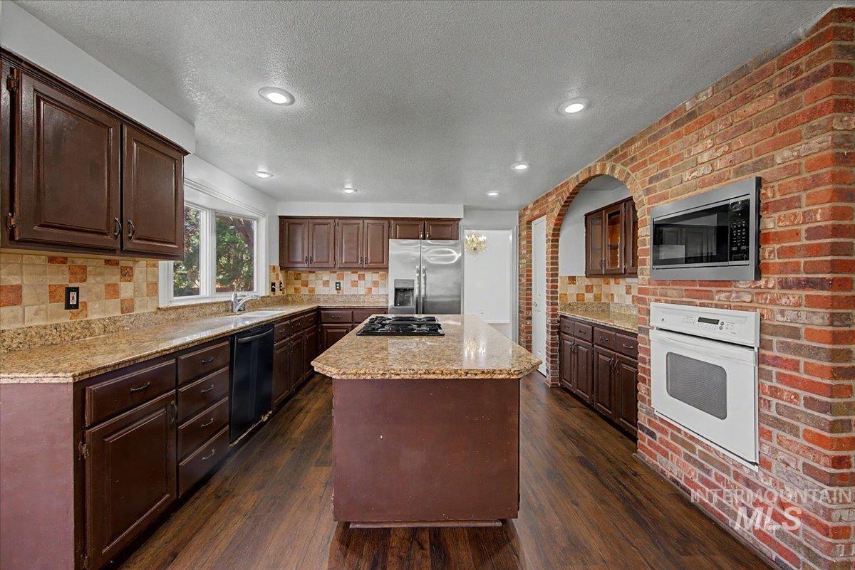Kitchen with dark wood finish cabinetry, a center island, stainless steel appliances, dark wood finished floors, and brick wall