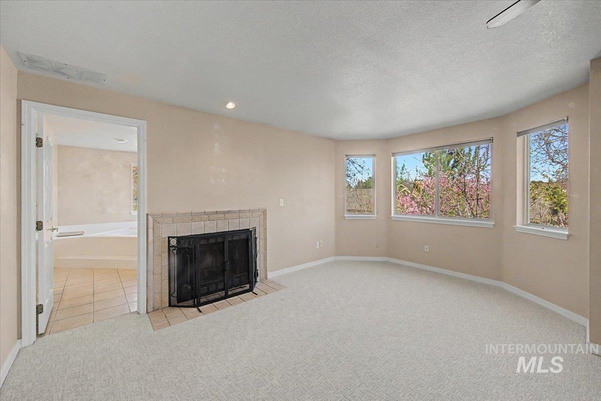 Unfurnished living room with light colored carpet, a fireplace, and a textured ceiling