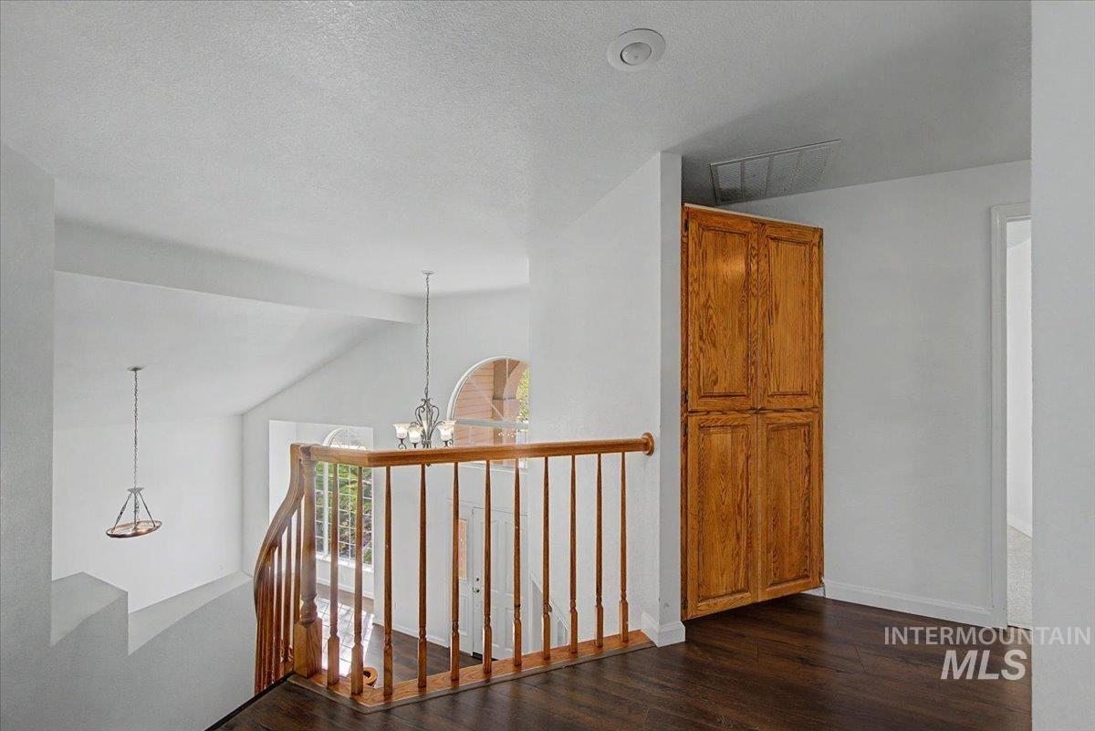 Hall with hanging lights, dark wood finished floors, and an upstairs landing
