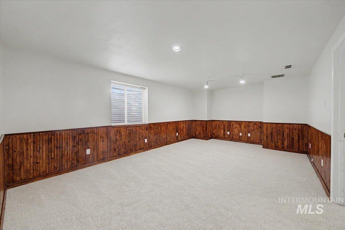 Spare room featuring light colored carpet, wainscoting, and wood walls