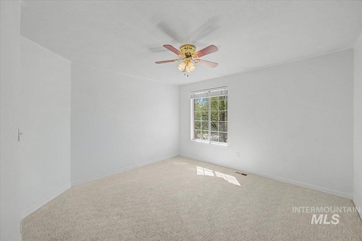 Carpeted spare room featuring ceiling fan and baseboards