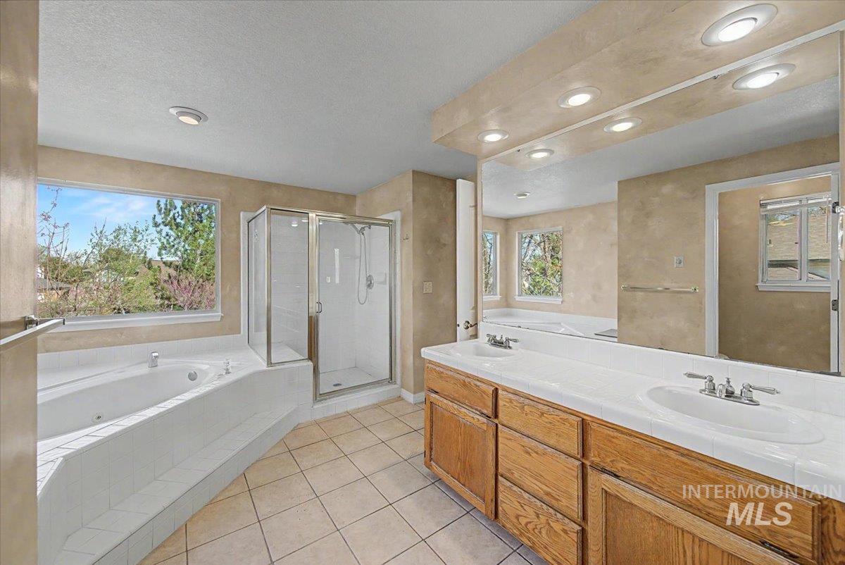 Full bath with a whirlpool tub, a shower stall, double vanity, light tile patterned flooring, and a textured ceiling