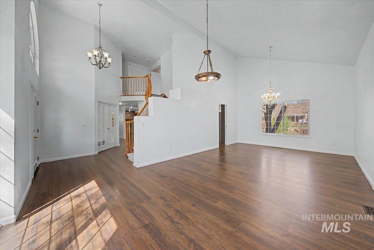 Unfurnished living room with suspended lighting, dark wood-type flooring, and lofted ceiling
