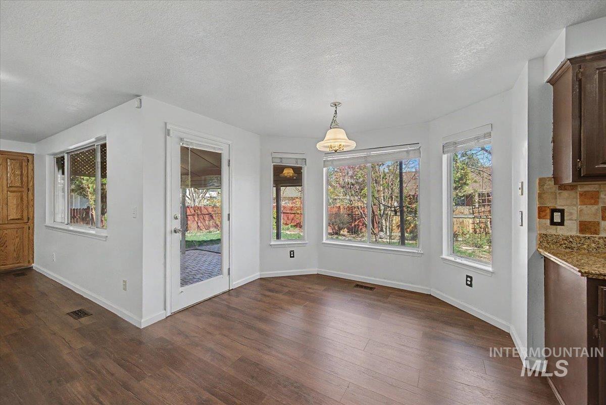 Unfurnished dining area featuring a textured ceiling and dark wood-style flooring
