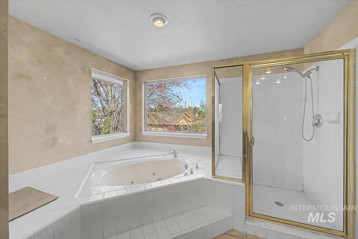 Full bathroom featuring a shower stall, a whirlpool tub, a textured ceiling, and a textured wall