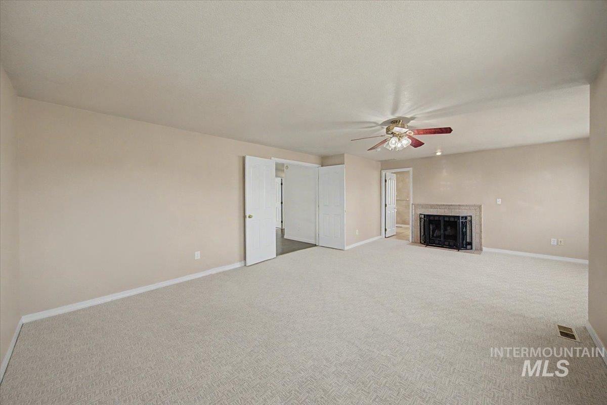 Unfurnished living room with a ceiling fan, light colored carpet, a fireplace with flush hearth, and a textured ceiling