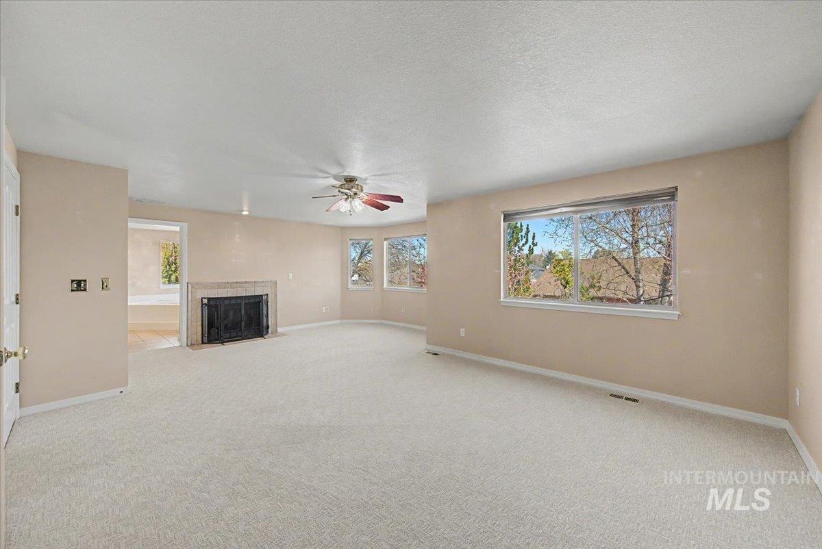 Unfurnished living room featuring light carpet, a fireplace with flush hearth, a ceiling fan, plenty of natural light, and a textured ceiling