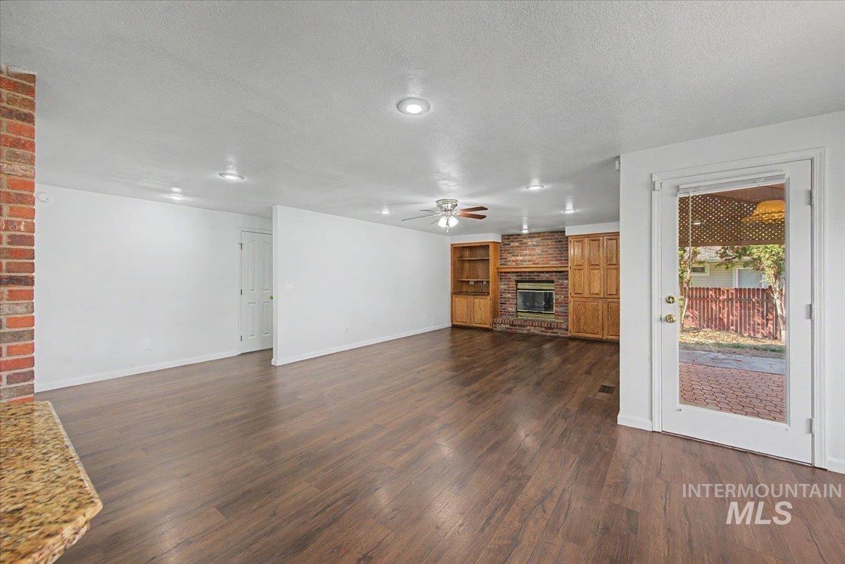 Unfurnished living room with a fireplace, dark wood-type flooring, a textured ceiling, and a ceiling fan