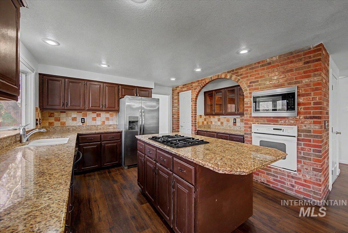 Kitchen with stainless steel appliances, a center island, dark wood finish cabinetry, light stone counters, and a textured ceiling