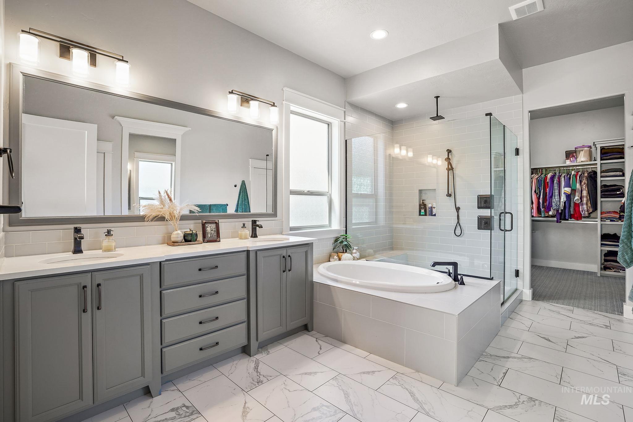Featuring large walk-in shower, soaker tub, double vanity and light marble finish floors