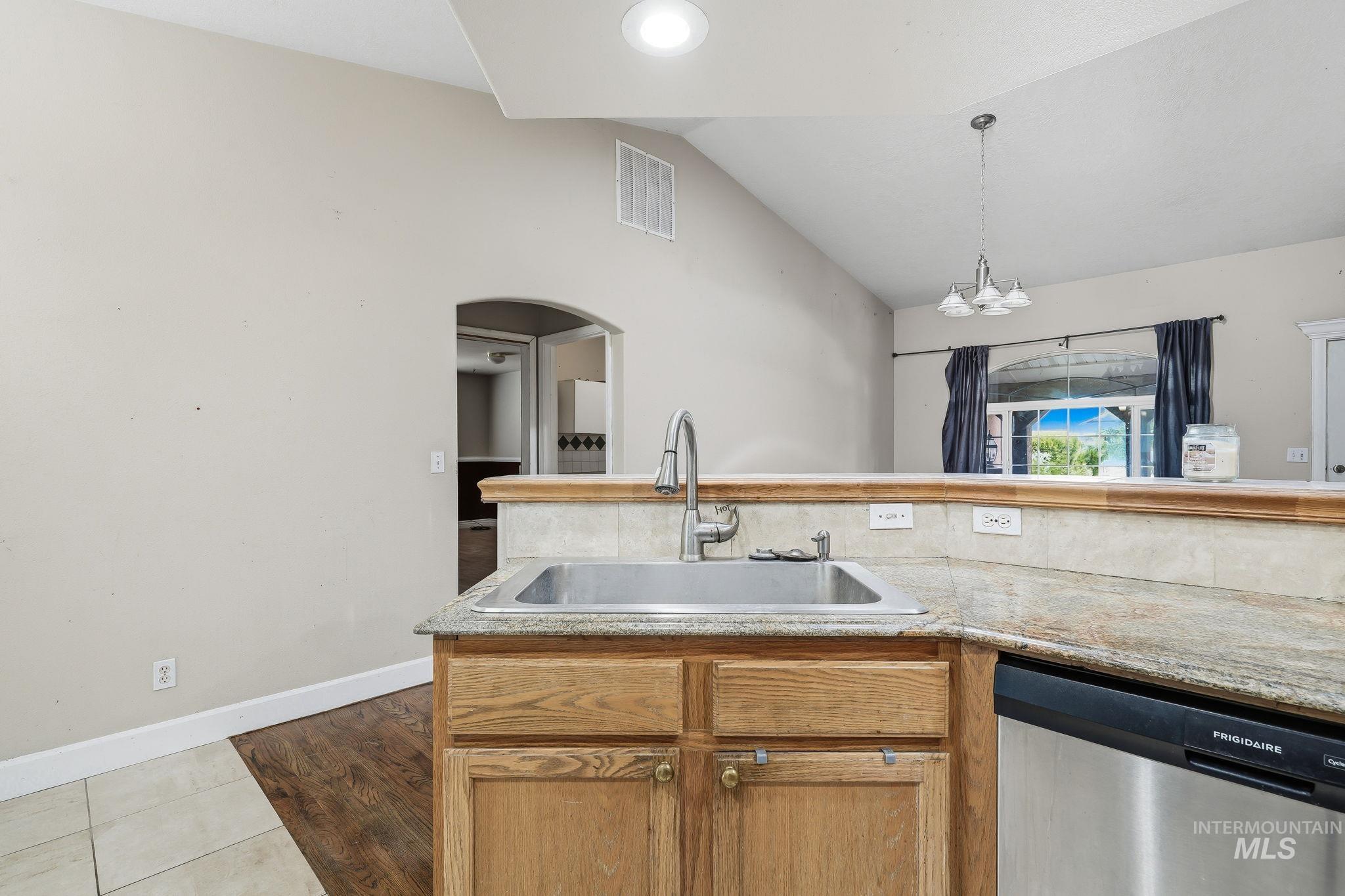Kitchen featuring a stainless steel sink, wood cabinetry, stone-look countertops, and a built-in stainless steel dishwasher