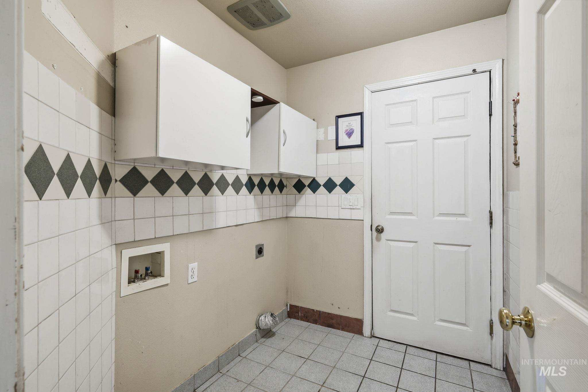 Laundry area featuring a paneled door, white cabinetry, and a tiled floor