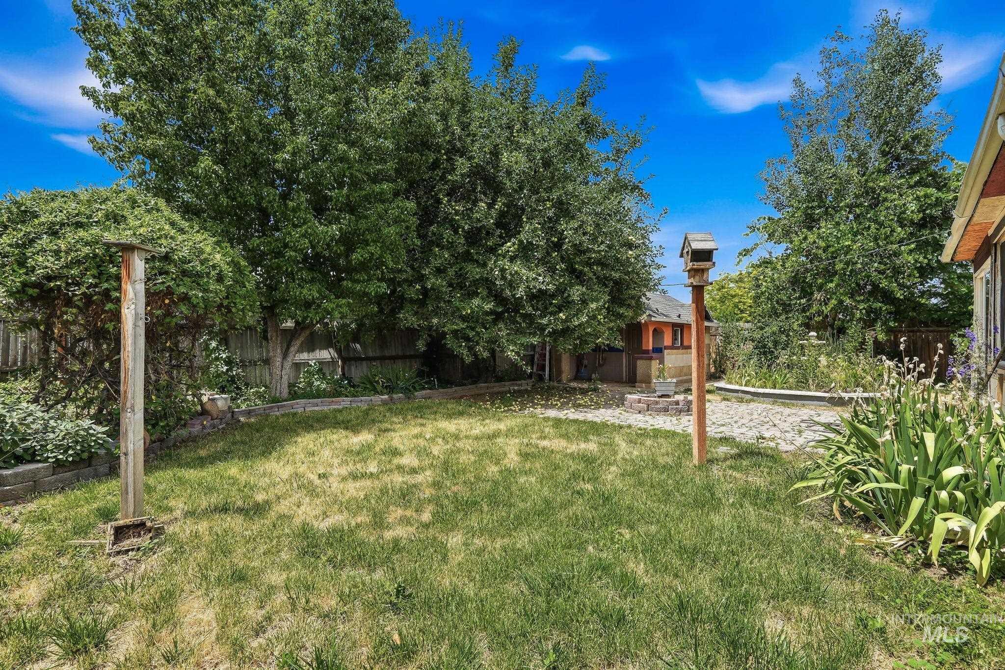 Enclosed backyard featuring a grass lawn, mature trees, and a paver patio area